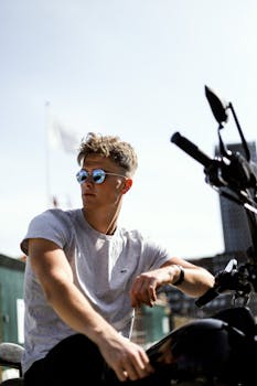 Young man with sunglasses posing on a motorcycle in Copenhagen, enjoying a sunny day outdoors.