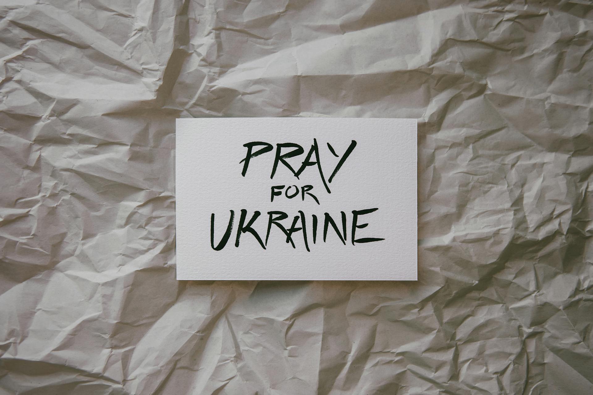 A card with 'Pray for Ukraine' on crumpled paper background, promoting solidarity.