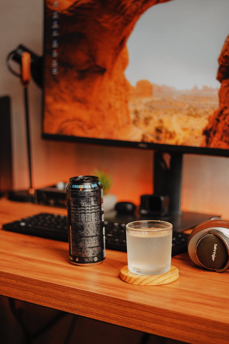 A Glass Of Cold Drink On A Wooden Desk With A Can And Computer