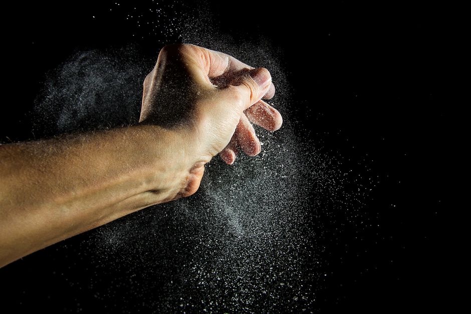 Close-up of a hand clapping with powder creating a dramatic effect against a black background.