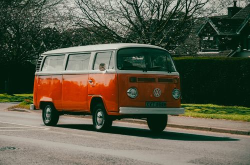 Free Classic orange Volkswagen van parked outdoors on a sunny road with trees and houses. Stock Photo