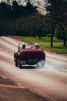 A classic vintage car with elderly passengers cruising down an open road on a sunny day.