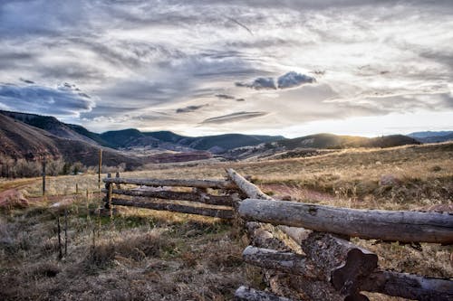 Brown Log Fence on Green Grass Field Under White Clouds