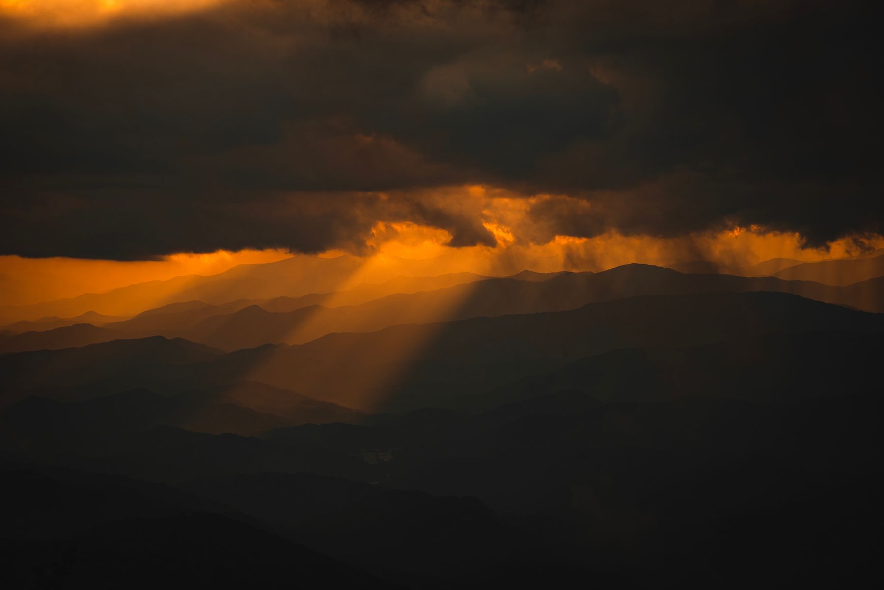 Ein einzelner Strahl des letzten Lichts fällt in der Abenddämmerung durch die Wolken auf gestaffelte Bergrücken