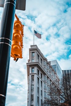 Vertical shot of a city building with American flag and traffic light under a cloudy sky.