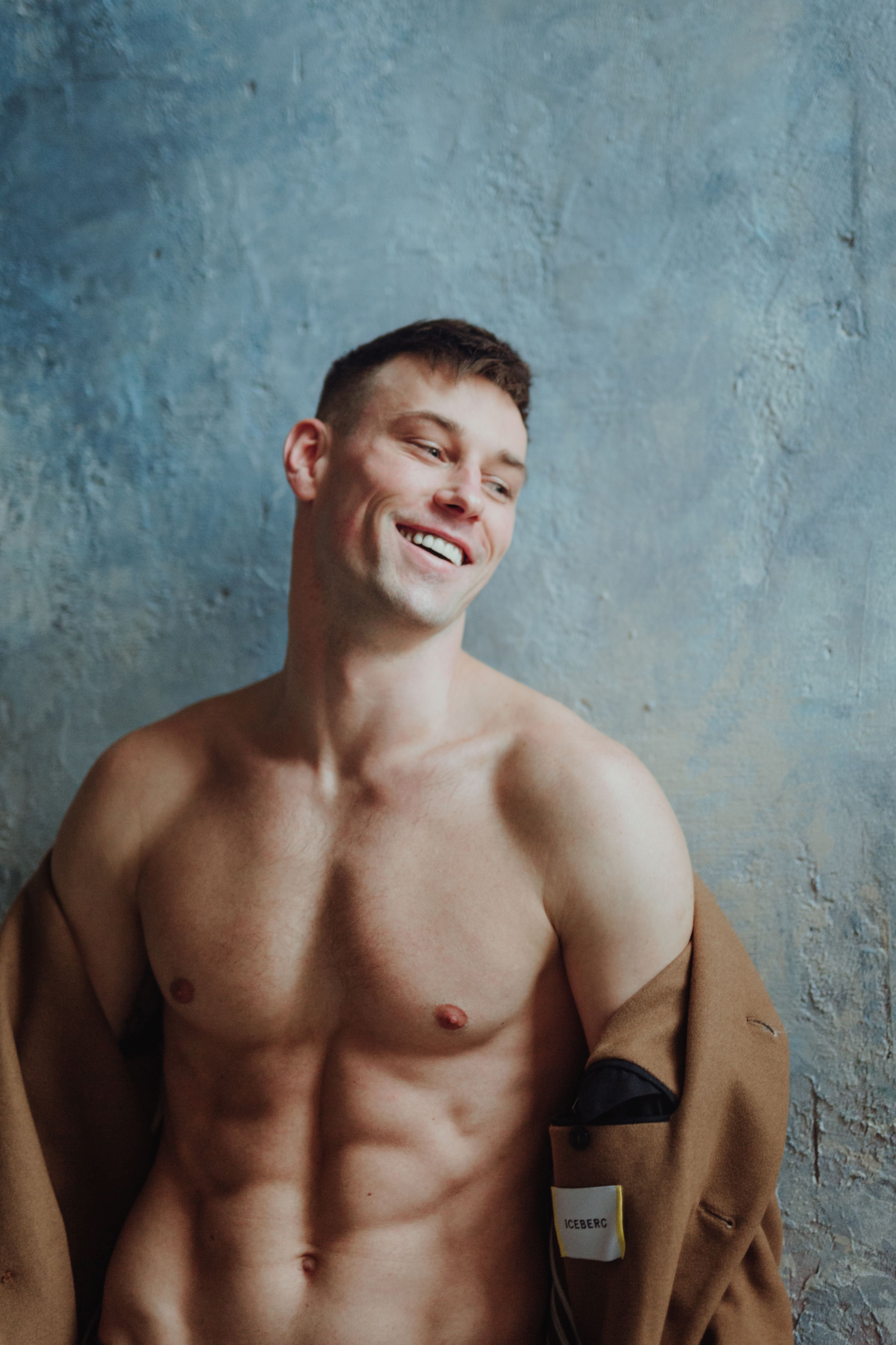Portrait of a smiling man with a muscular physique and short hair against a textured blue background.