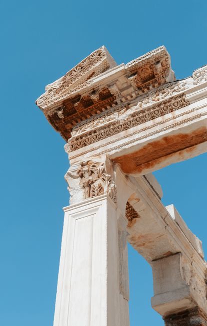 Detailed view of ancient Roman architecture with ornate carvings set against a vibrant blue sky.