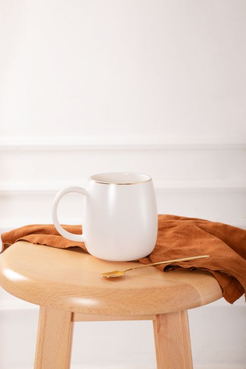Free Minimalist white mug on a wooden stool with a copper spoon and cloth, perfect for kitchen decor. Stock Photo