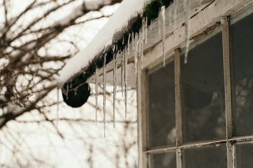 Free Close-up of icicles hanging from a snow-covered rooftop, emphasizing winter's chill. Stock Photo