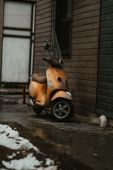 A single yellow scooter parked in an urban alley during a snowy winter day.
