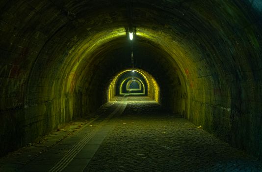 A dimly lit stone tunnel with eerie greenish lighting creating an atmospheric feel.