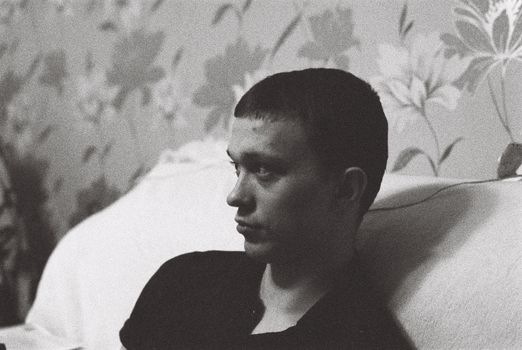 A man leans on a sofa, deep in thought, captured in striking black and white.