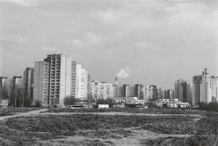 Grayscale Photo Of City Buildings Near A Vacant Lot With Grass