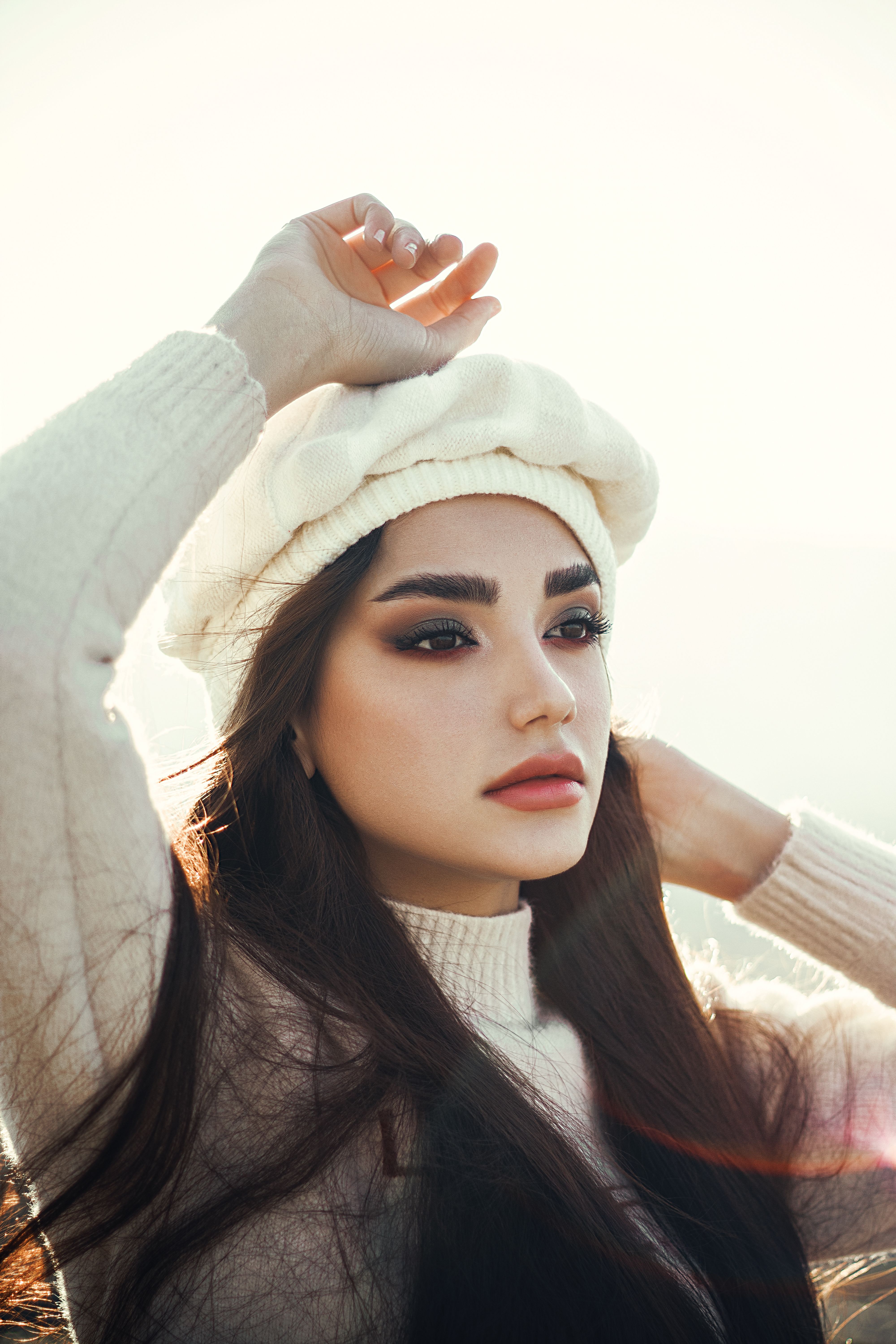 Stunning portrait of a woman in white sweater and beret with sunlight background.