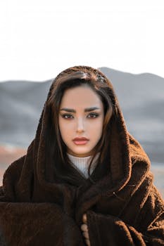 Portrait of a woman in a cozy fur coat outdoors against a mountain range.