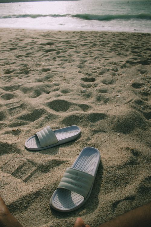 Free Pair of slippers on a sandy beach in Dubai under a warm sun, evoking a relaxed and serene atmosphere. Stock Photo