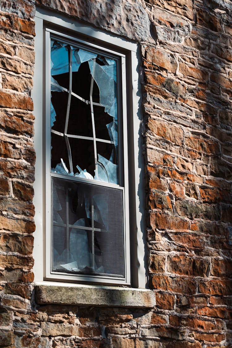 A Broken Glass Window On A Brown Brick Wall