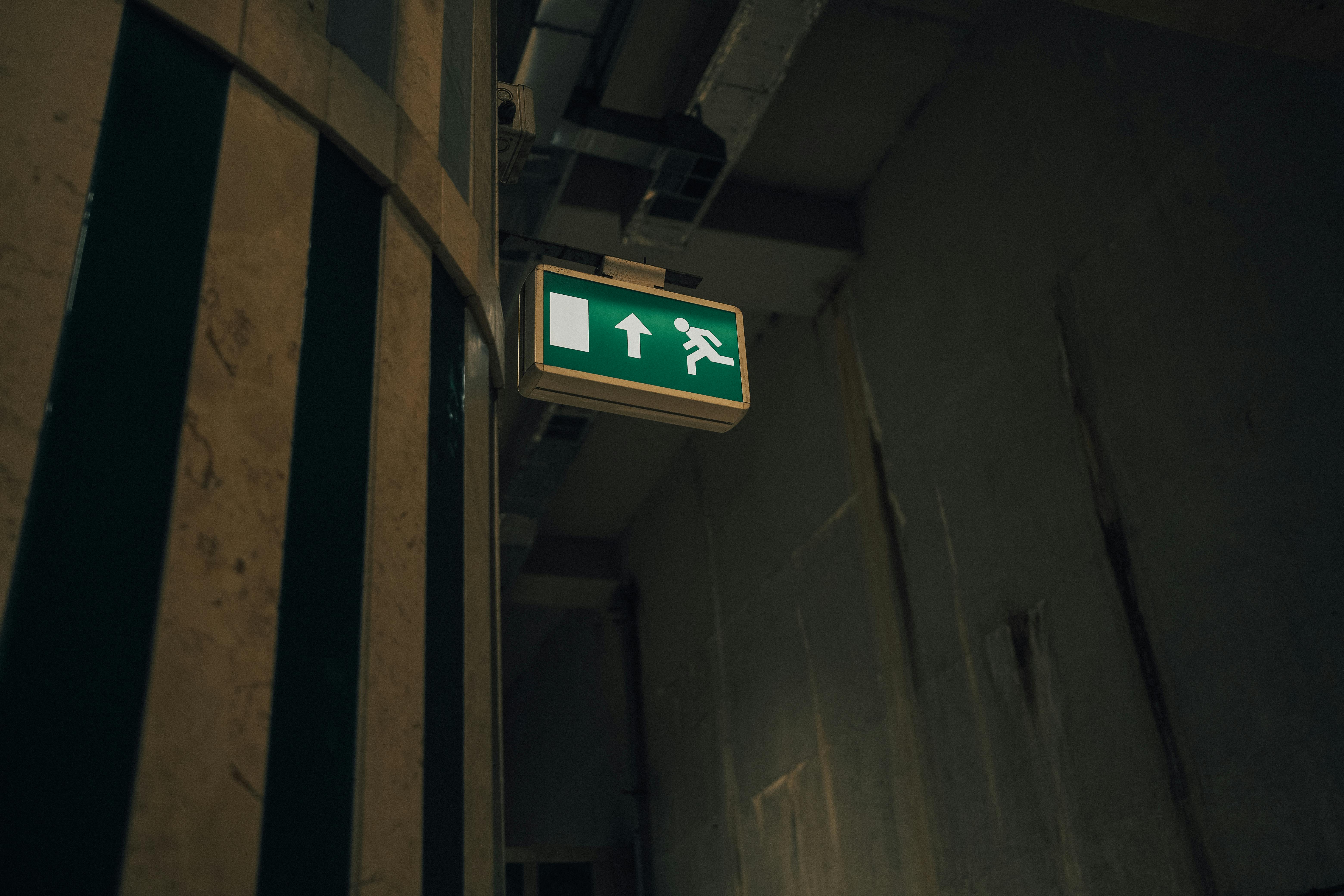 A dimly lit corridor with a green and white emergency exit sign indicating direction.