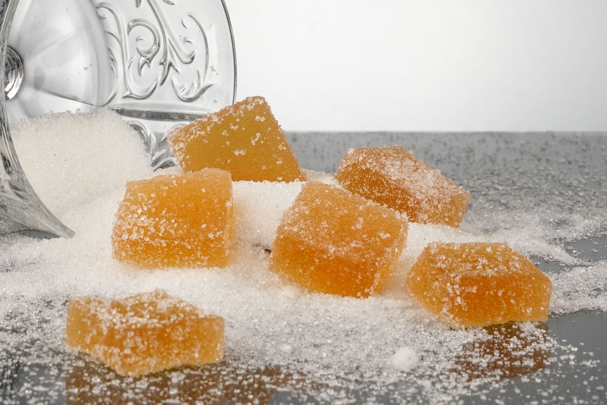 Close-up of sugar-coated jelly candies scattered from a glass, reflecting on a shiny surface.