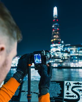 A photographer takes a shot of London's illuminated skyline at night, featuring The Shard.
