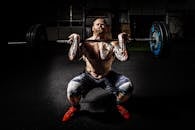 一名男子在健身房举哑铃深蹲，进行力量训练