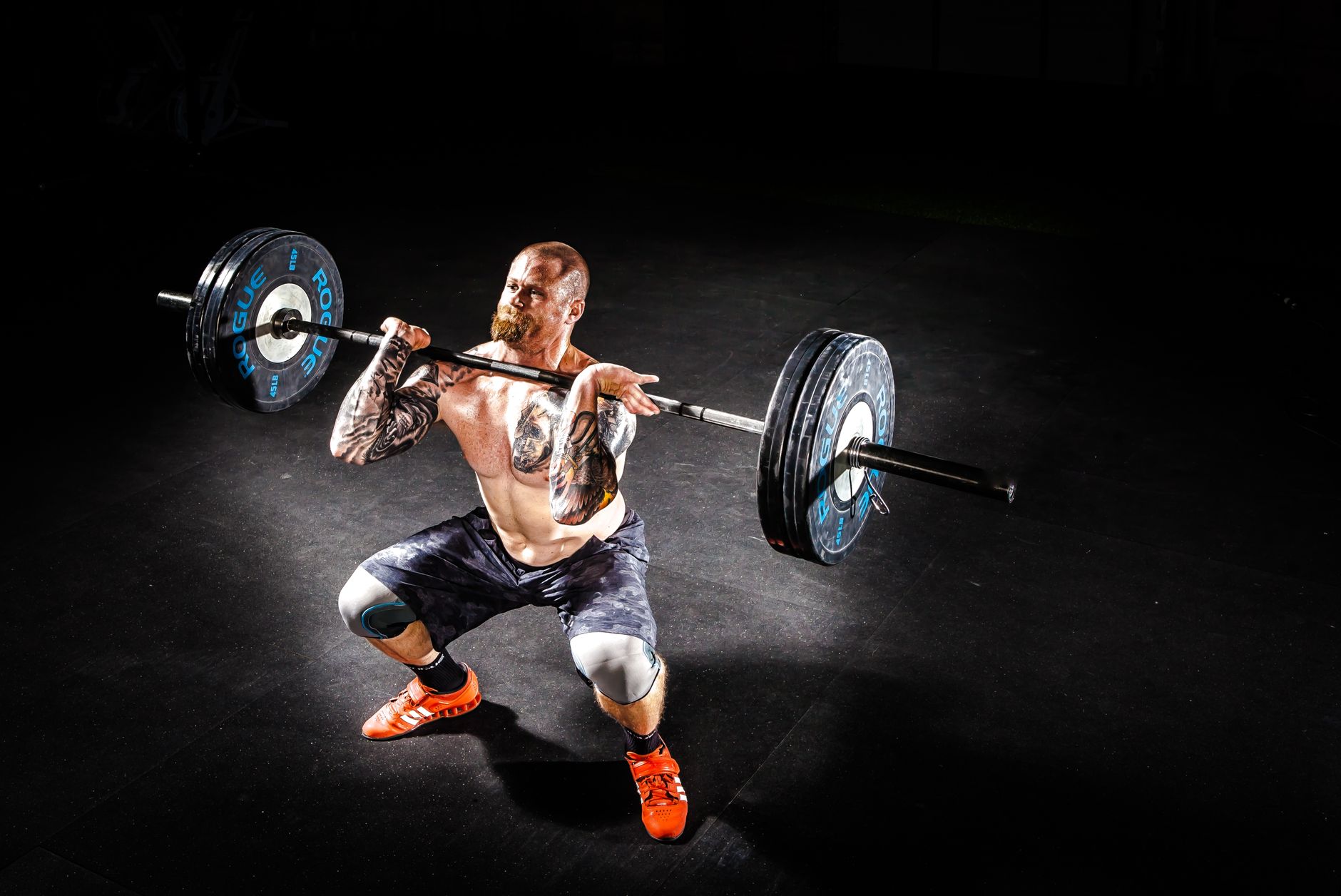 A muscular man performing a power clean exercise in a dimly lit gym.