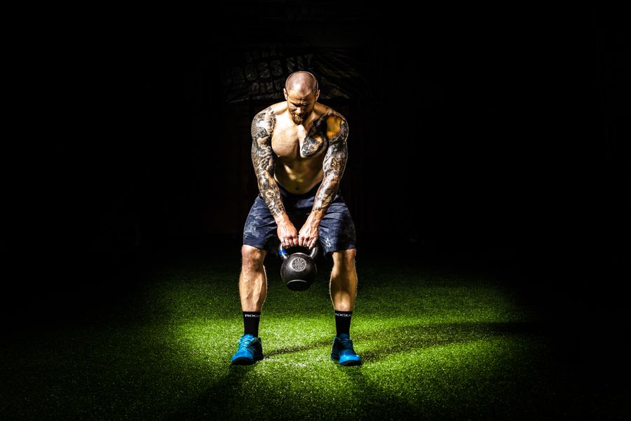 Adhérent avec deux kettlebells sur le sol sombre de la salle