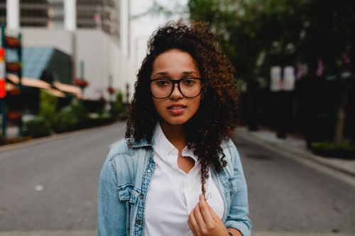 Free Young woman with curly hair and glasses posing on an urban street in a casual outfit. Stock Photo