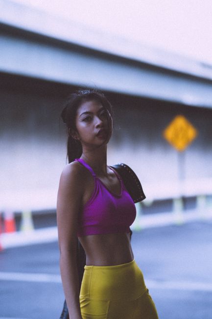 Portrait of a young woman in athletic wear under an urban overpass, radiating confidence and style.
