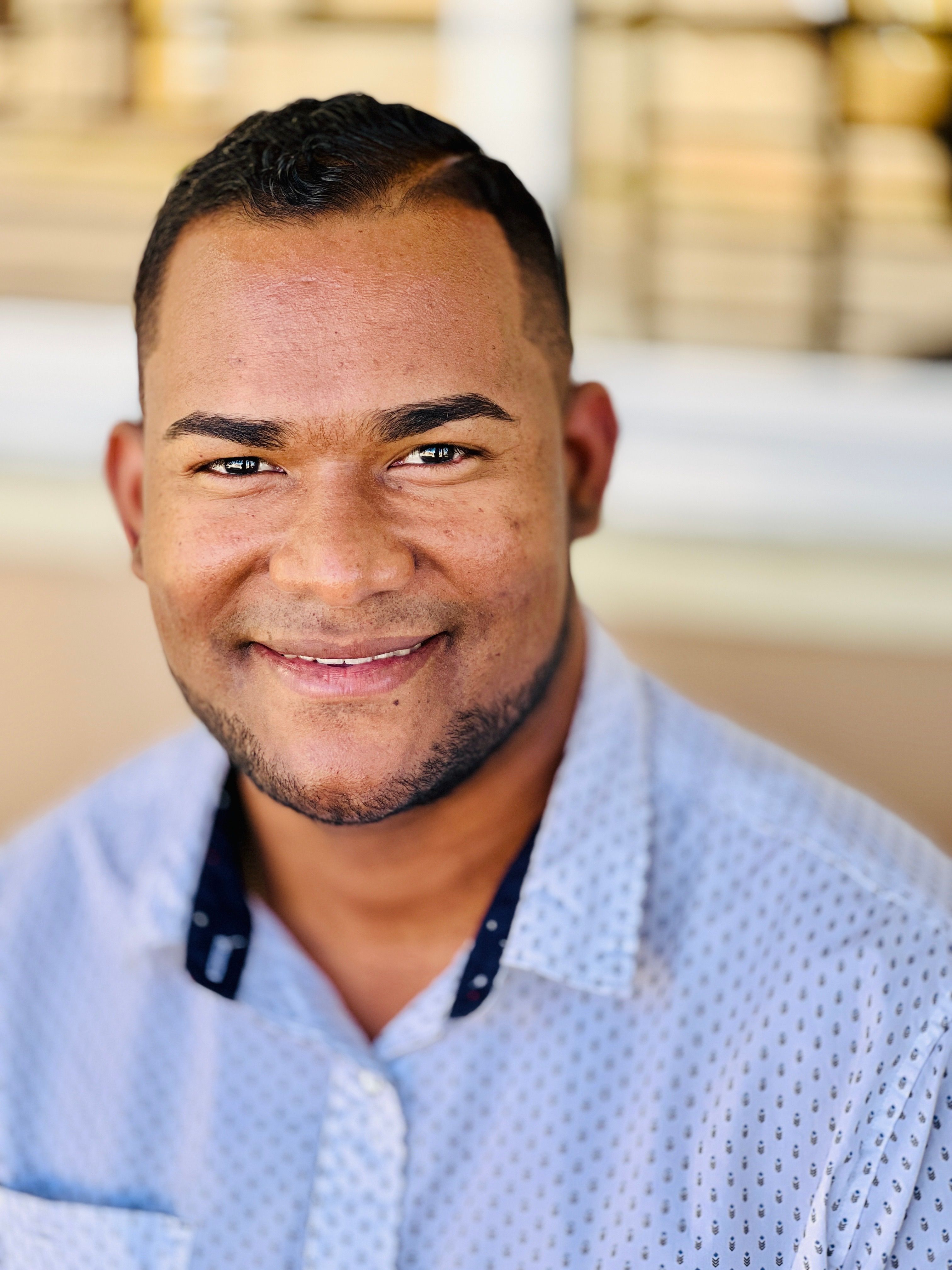 Portrait of a smiling man in a casual shirt sitting outdoors.