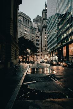 Moody street view of downtown skyscrapers reflecting on wet pavement at dusk.