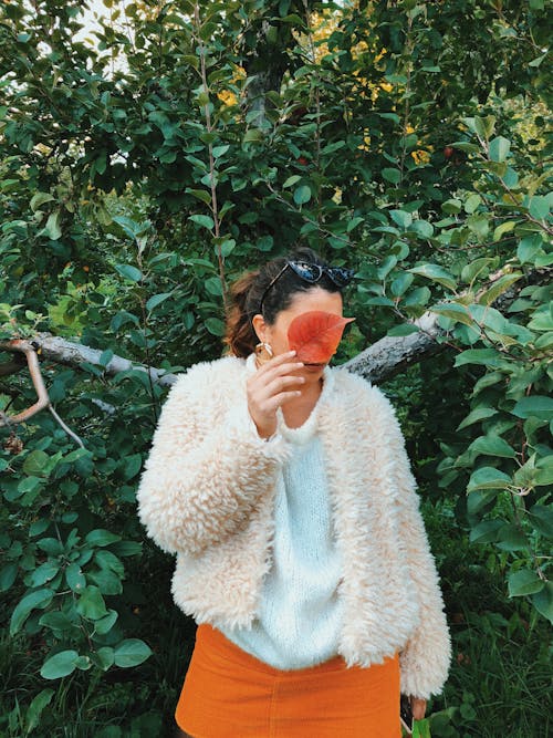 Woman in Faux-Fur Jacket Covering Face with Red Leaf