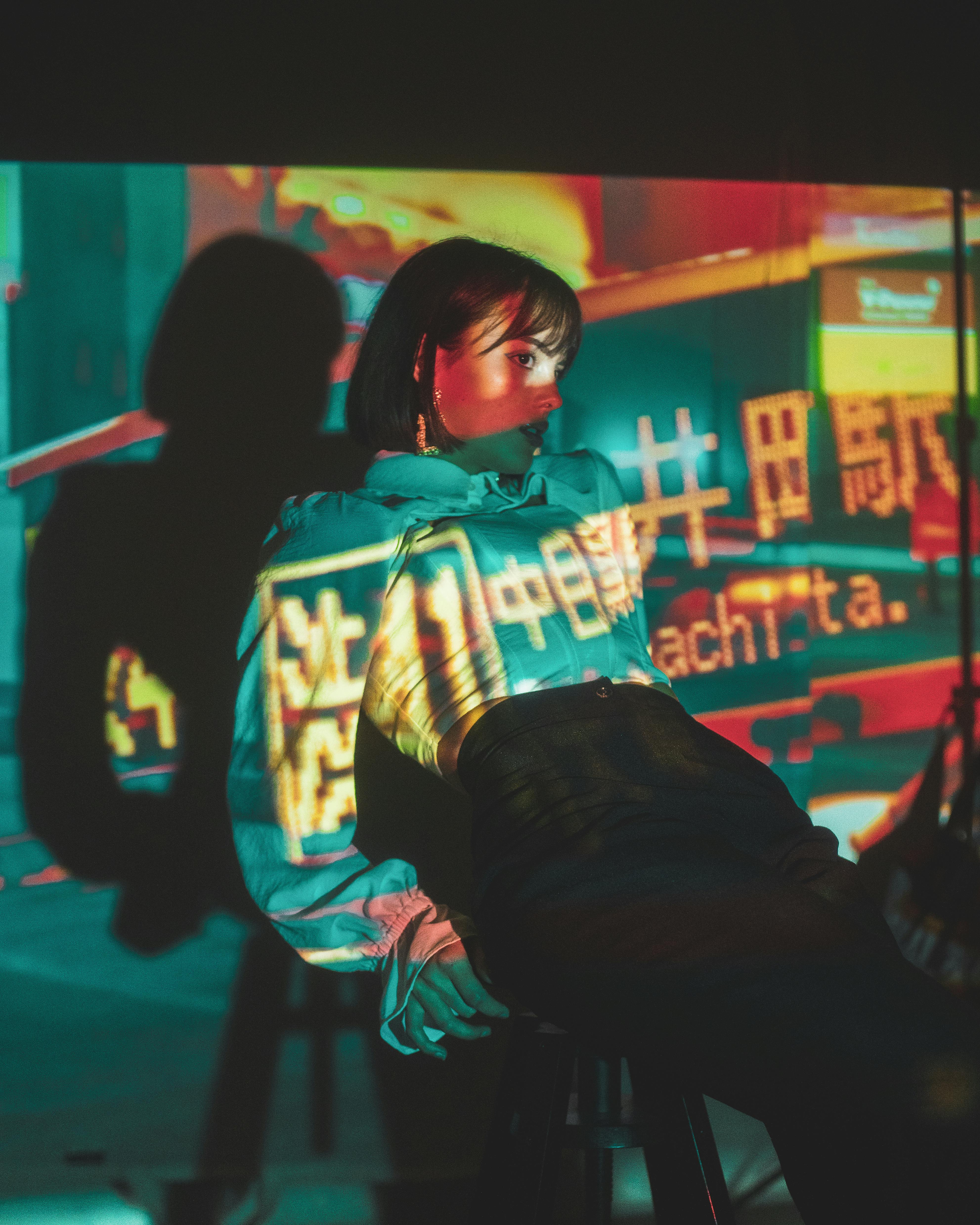 young woman illuminated by projector sitting on bar stool