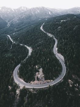 Stunning aerial view of a winding road cutting through a dense coniferous forest in mountainous terrain.