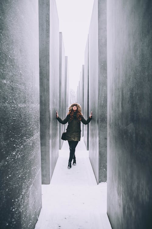 Woman in Black Jacket standing between Gray Walls 