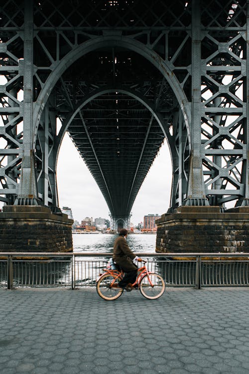 Free Man Riding Embankment Road under Bridge on Orange Bike  Stock Photo