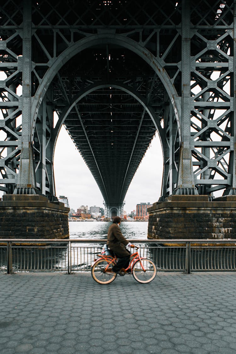 Man Riding Embankment Road Under Bridge On Orange Bike 