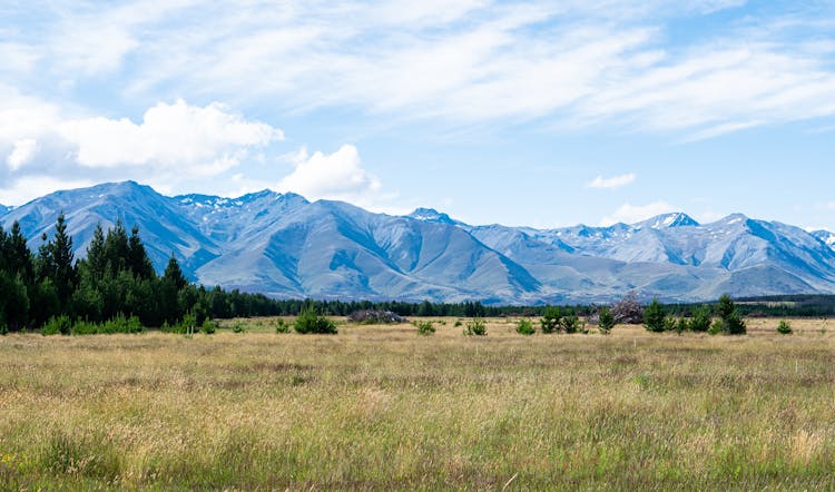 Grass Field Near Mountain Under Blue Sky