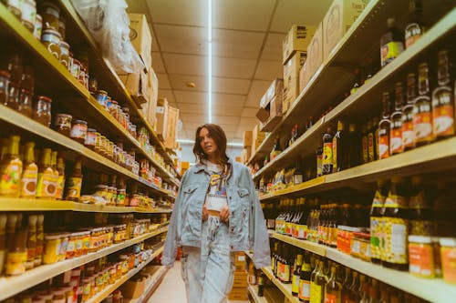 Girl in Denim Jacket and Jeans Walking Along Shop Shelves