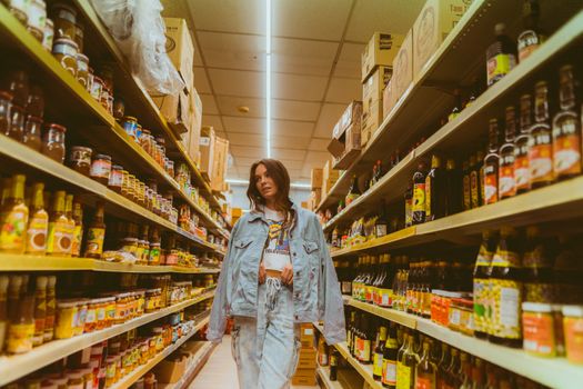 Woman in denim browsing grocery store aisle with products on shelves.