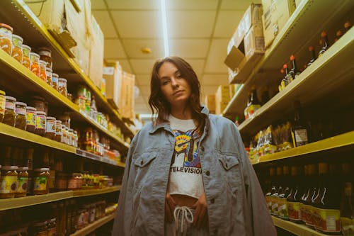 Stylish Woman in Denim Jackets standing between Shelves 