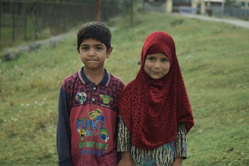 Free A boy and a girl smiling happily in a green grass field. Stock Photo
