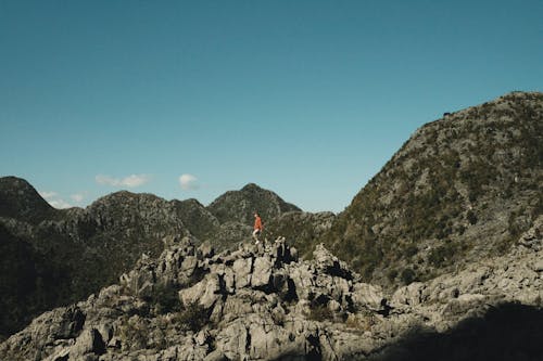 A Person Standing on a Rocky Cliff Beside a Mountain