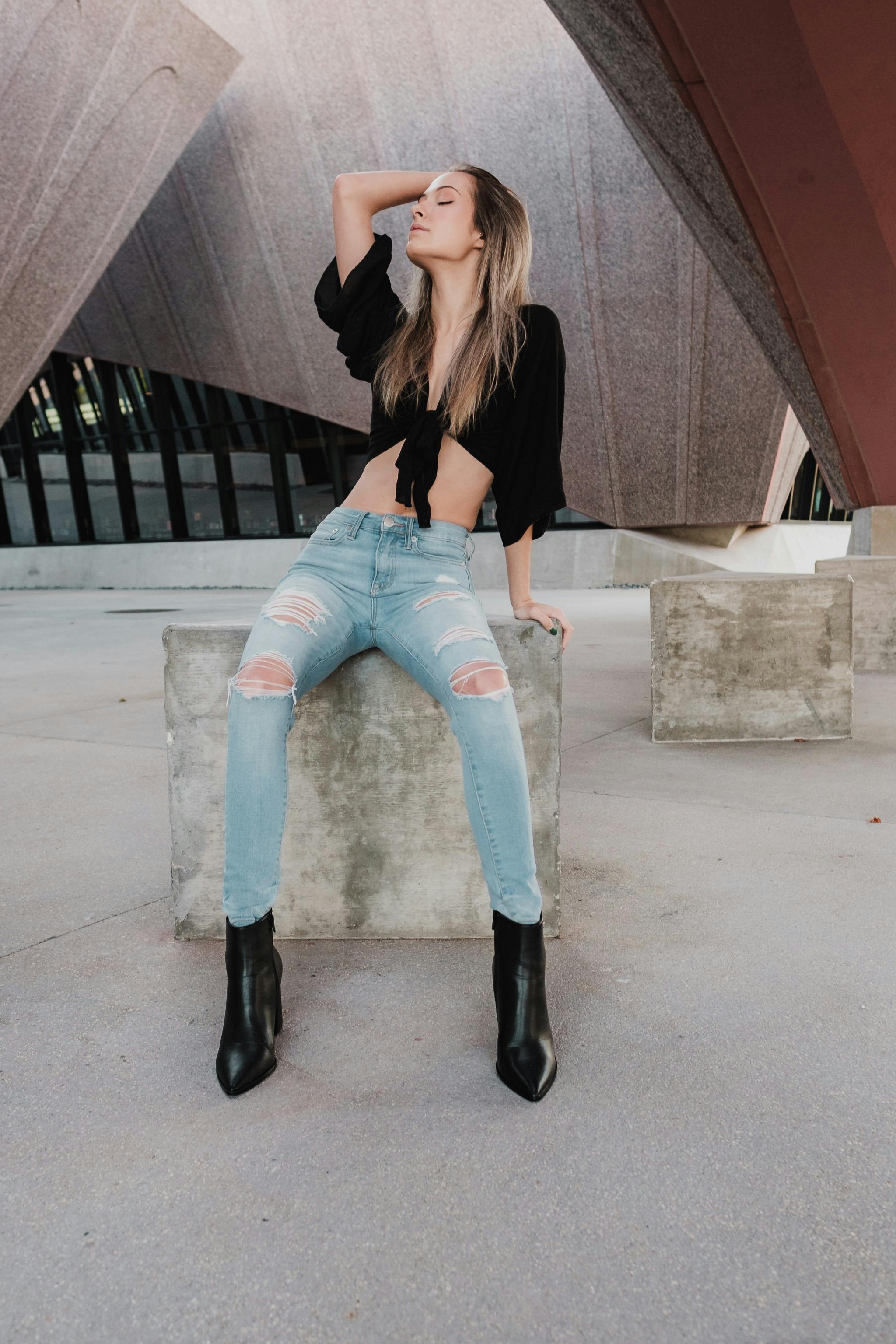 Woman in Black Crop Top and Blue Denim Jeans Sitting on Concrete