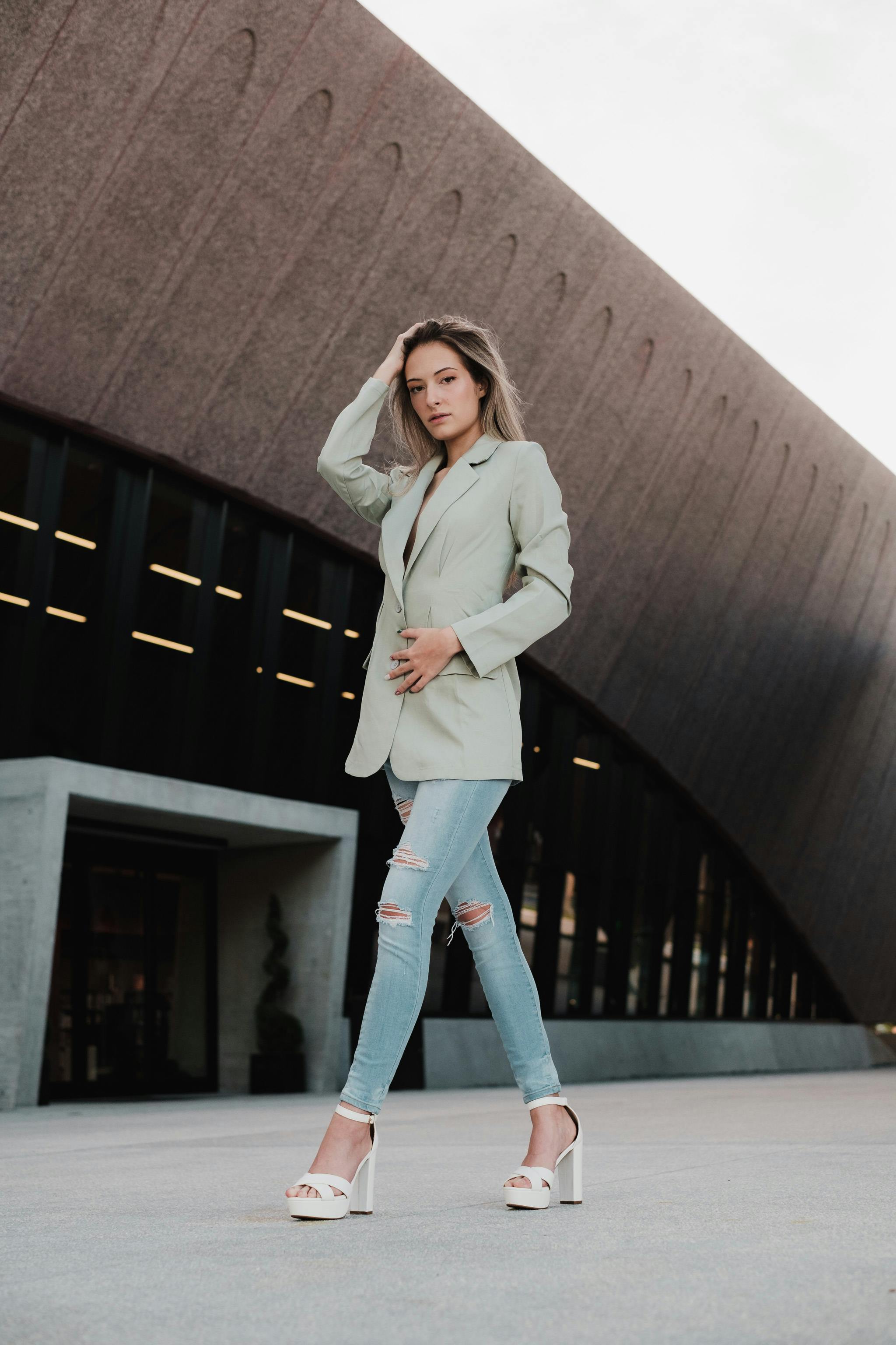 Stylish woman poses confidently outdoors showcasing modern fashion against architectural backdrop.