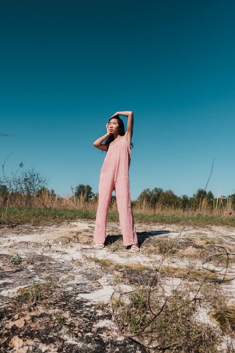 Woman Posing In Pink Overalls Outfit Standing On Dry Grass Field