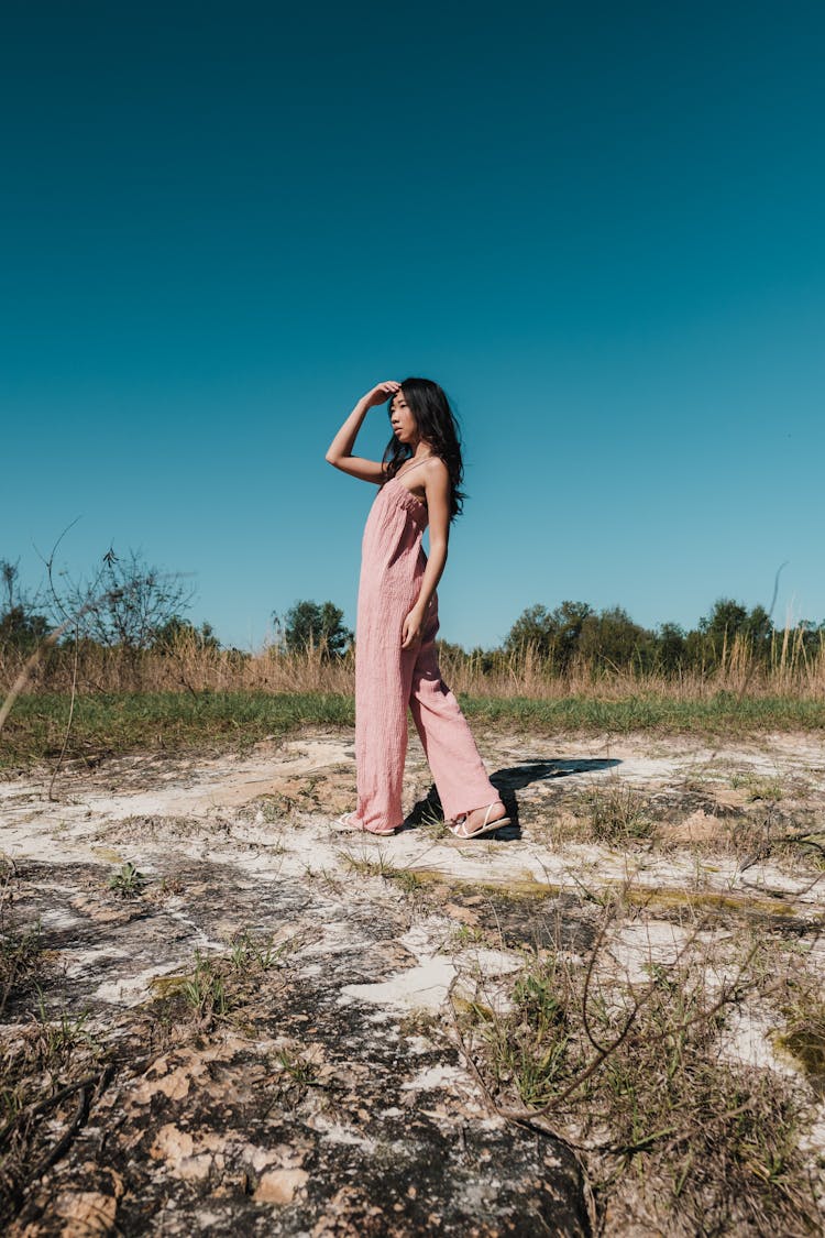 A Woman In Pink Jumpsuit Standing On A Vacant Lot