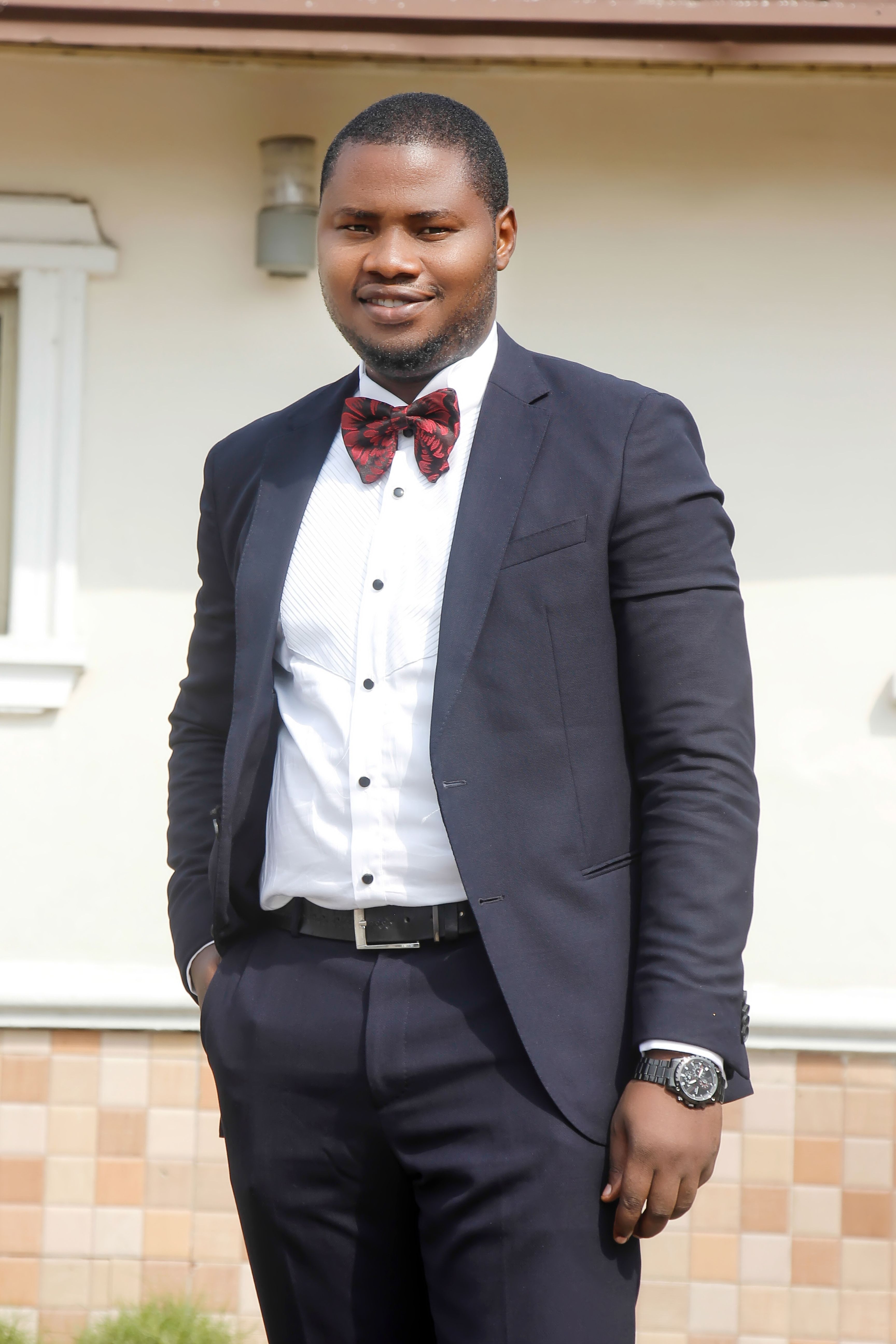 Elegant portrait of a man in a black suit and bowtie standing outdoors in Abuja.