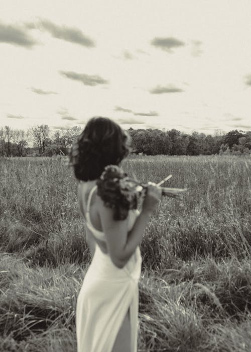 Grayscale Photo of Woman Holding Bouquet of Flowers Standing on Grass Field