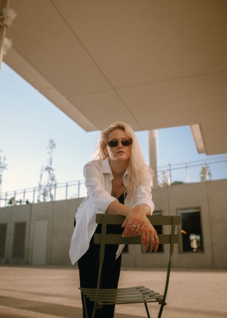 Blonde woman in sunglasses posing with a chair outdoors in Des Moines.